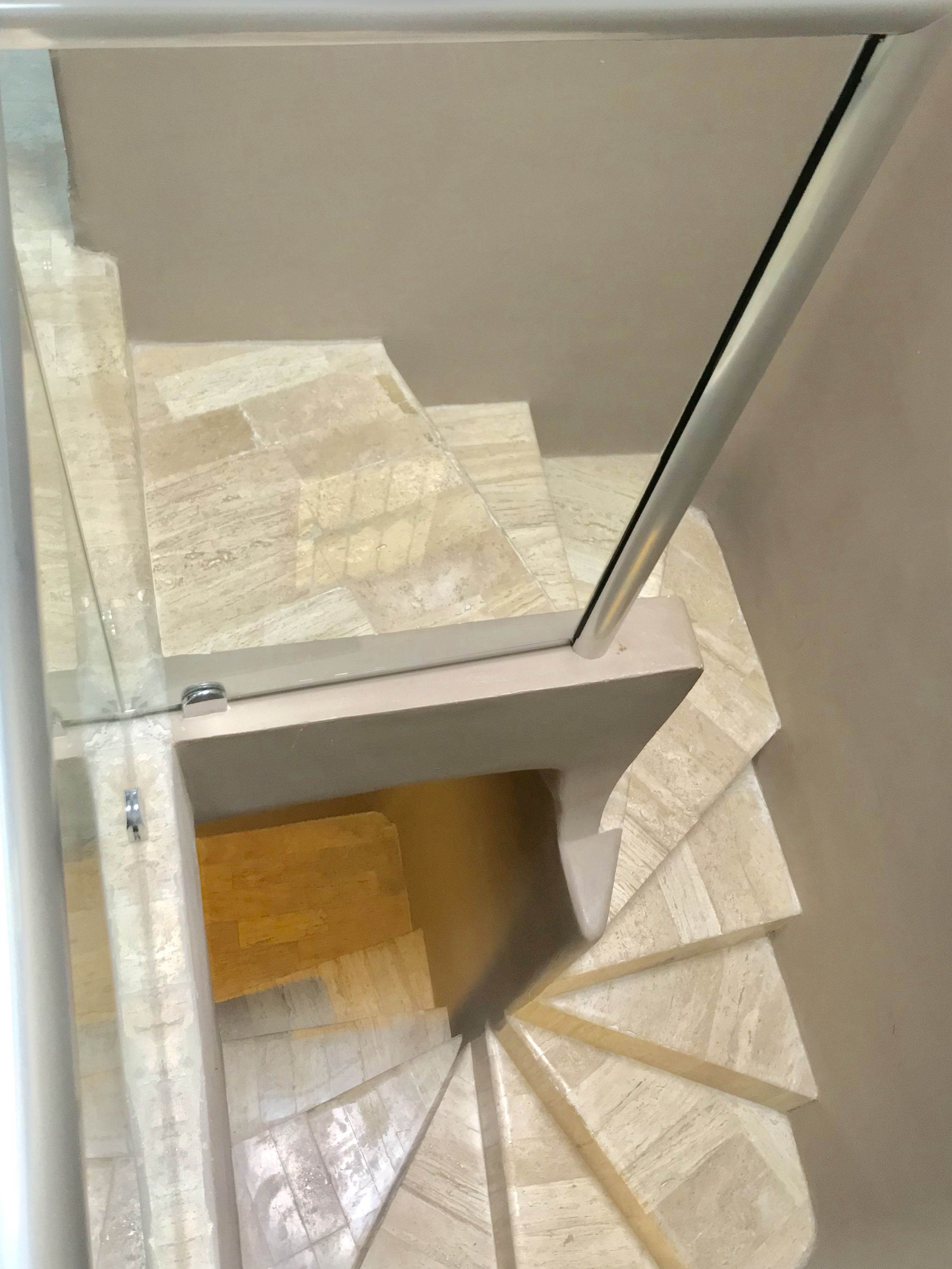 A spiral staircase with a modern design, made of light-colored stone tiles.