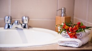 Une salle de bain avec un lavabo blanc, un porte-savon en bois et une pile de serviettes blanches ornées de fleurs rouges.