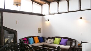 Un intérieur rustique avec des poutres apparentes, un escalier en bois, un canapé agrémenté de coussins colorés et un luminaire suspendu.