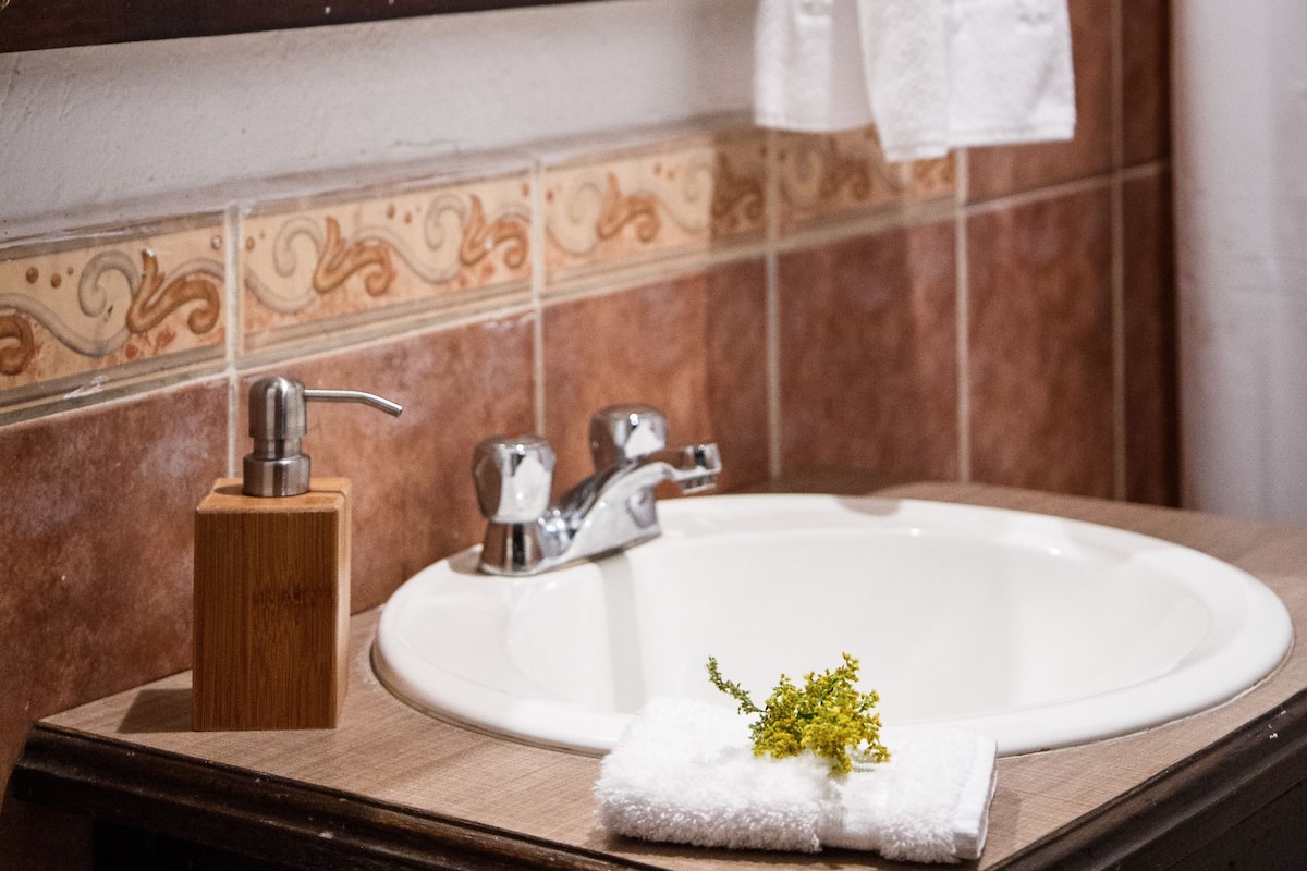 Un baño con lavamanos, espejo y toallero.