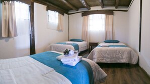 Une chambre avec deux lits, chacun recouvert d’une couverture bleue et agrémenté d’un oreiller blanc. On y trouve des fenêtres avec des rideaux, des poutres en bois au plafond et un plancher en bois.