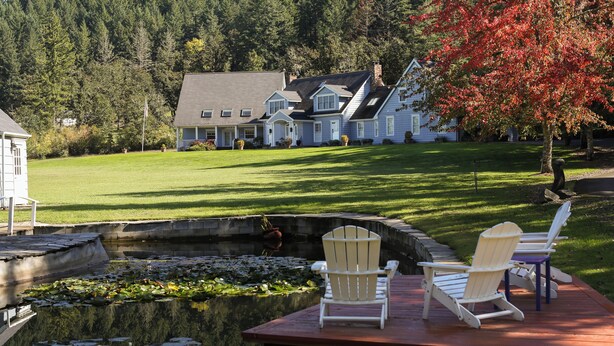 A lakeside deck with Adirondack chairs, a pond with lily pads, and a large house in the background. - Spacious Country Guest Apartment (Eugene)