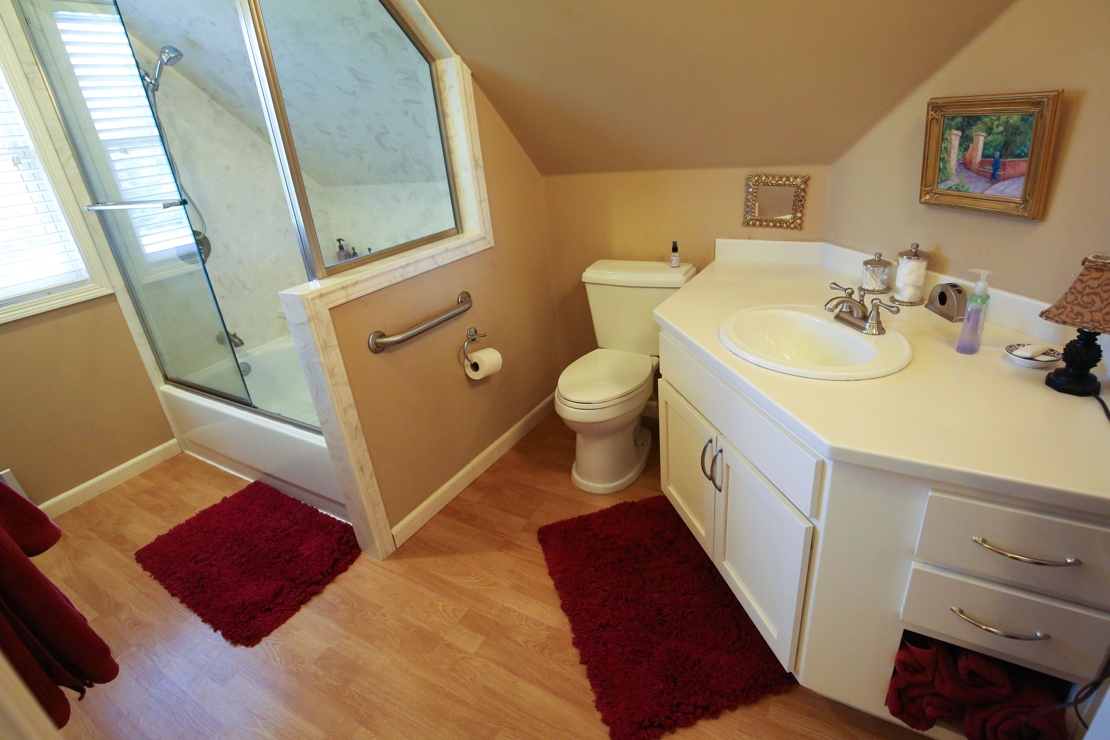 A bathroom with a glass shower enclosure, a toilet, a sink with a mirror, and a vanity with drawers.