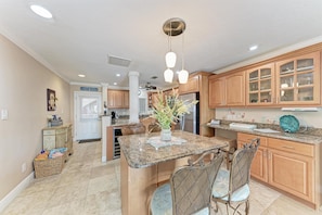 A kitchen with granite countertops, wooden cabinets, a central island with seating, pendant lighting, and a refrigerator. - Siesta Key's PREMIER LOCATION with amazing beach view! (SIESTA KEY)