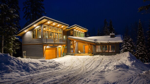 Une grande maison à plusieurs étages, dotée d’un porche abrité et d’un toit recouvert de neige, entourée de neige et d’arbres.