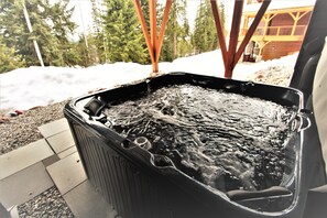 Un jacuzzi al aire libre con una terraza de madera y nieve de fondo.