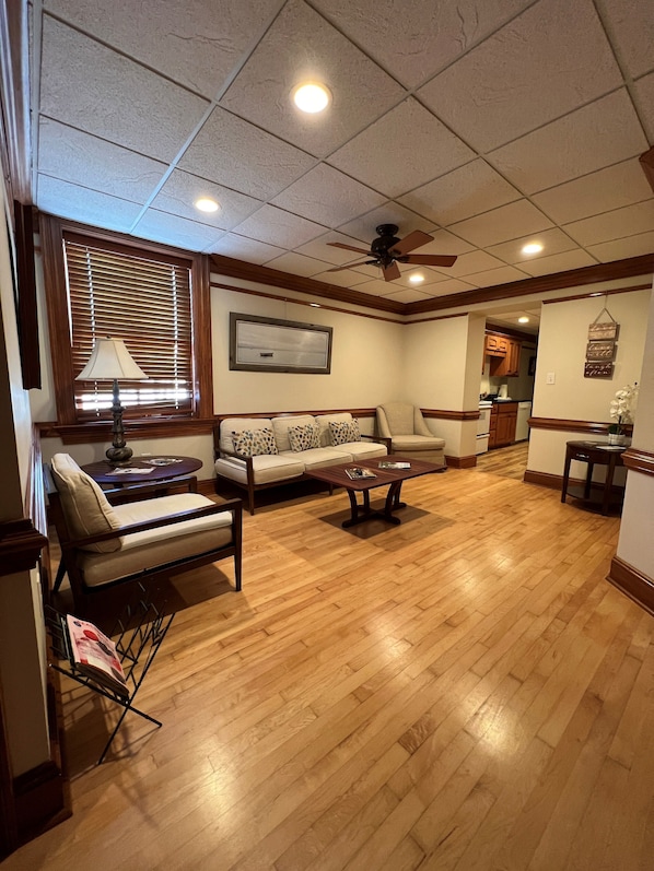 A spacious living room with a wooden floor, a sofa, a coffee table, and a ceiling fan.