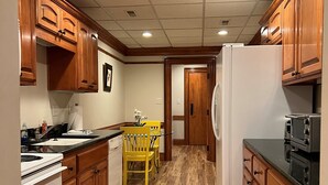 A kitchen with wooden cabinets, a white refrigerator, a stove, and a dining area with yellow chairs. - Historic Downtown Condo-1 Bedroom (New Bern)