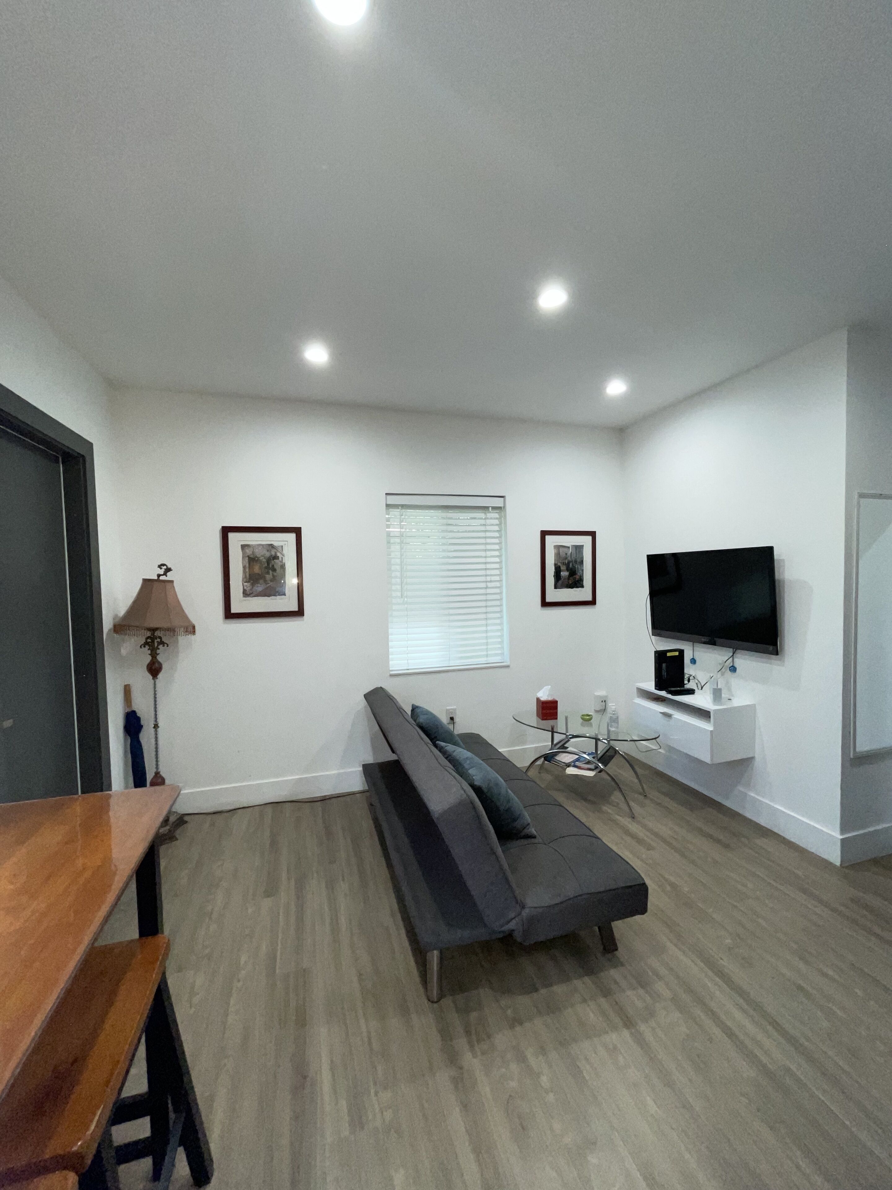 A modern living room with a sofa, a TV mounted on the wall, and a wooden table.