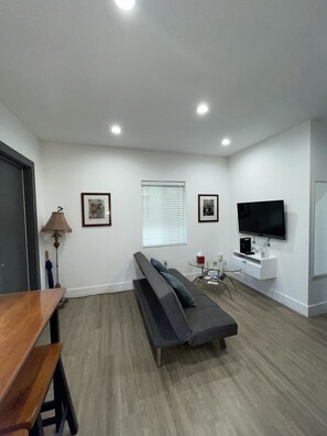 A modern living room with a sofa, a TV mounted on the wall, and a wooden table.