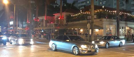A nighttime city street with cars, palm trees, and tall buildings.