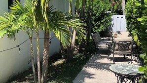 En terrasse med en støbt sti, udendørs møbler og forskellige tropiske planter.