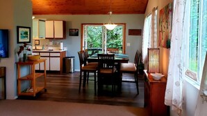 A spacious living area with a wooden ceiling, a dining table with chairs, a kitchen area, and large windows with curtains. - Tropical Vacation Home in Hawaiian Beaches, Pahoa, HI (Pahoa)
