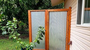 A wooden fence with a corrugated metal door, a potted plant, and a house with a window. - Tropical Vacation Home in Hawaiian Beaches, Pahoa, HI (Pahoa)