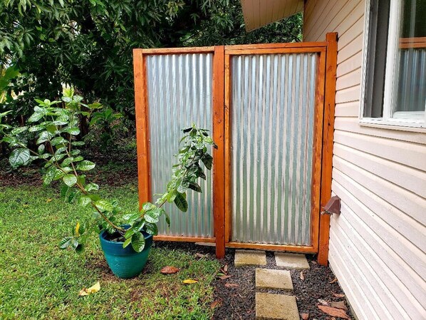 A wooden fence with a corrugated metal door, a potted plant, and a house with a window. - Tropical Vacation Home in Hawaiian Beaches, Pahoa, HI (Pahoa)