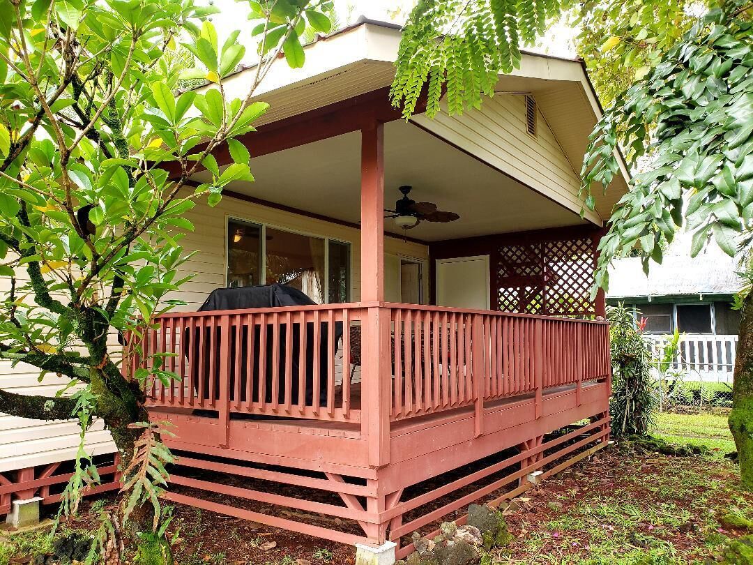 A covered porch with a red railing, a ceiling fan, and a view of a house in the background.