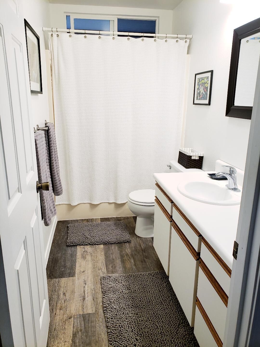 Et badeværelse med et hvidt badekar, toilet, håndvask og bruseforhæng.