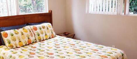 A bedroom with a bed, a ceiling fan, and two windows with blinds.