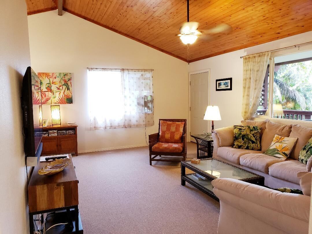 A living room with a wooden ceiling, a sofa, a chair, a coffee table, a TV, and a painting.