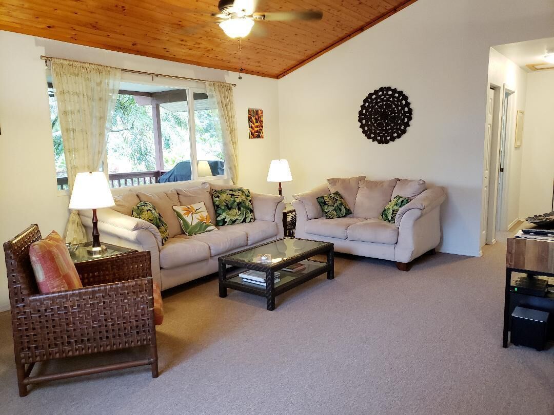 A living room with two sofas, a coffee table, a wicker chair, and a ceiling fan.