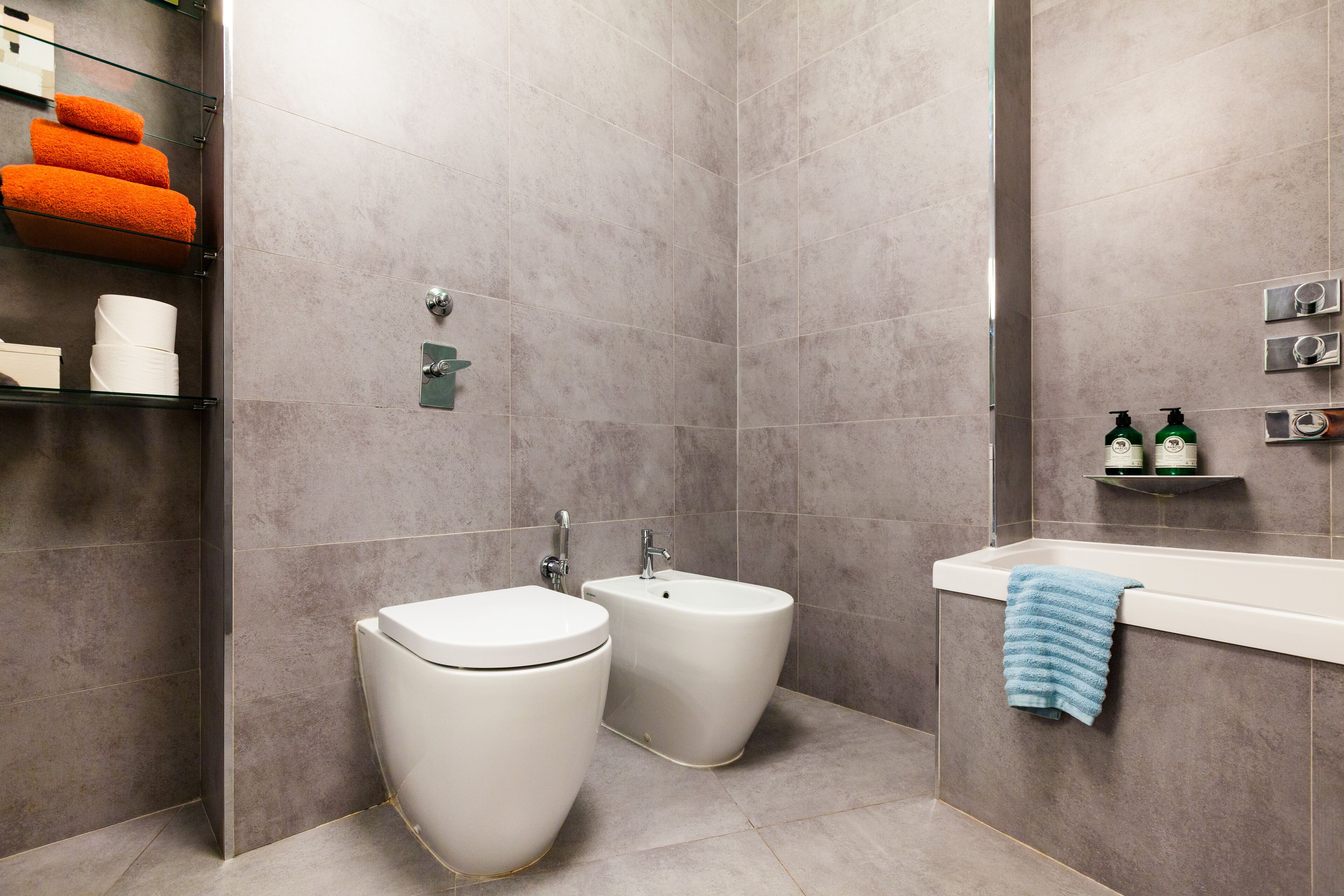 Une salle de bain moderne avec deux toilettes, un bidet, une baignoire et des étagères contenant des articles de toilette.