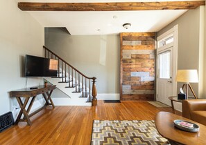 A living room with a wooden staircase, a flat-screen TV, a wooden coffee table, and a patterned rug.