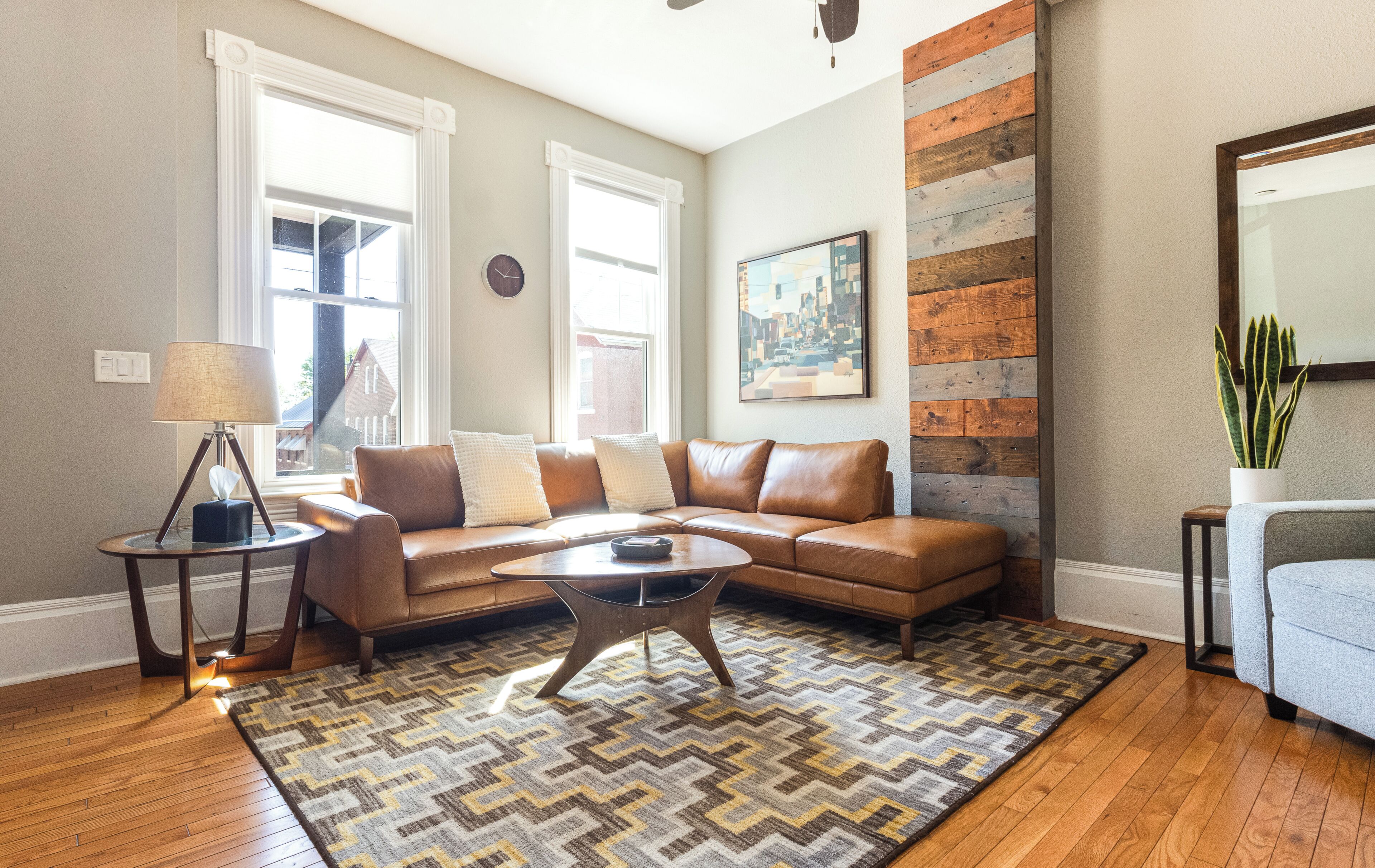 A living room with a leather sofa, a coffee table, a patterned rug, and a wooden accent wall.