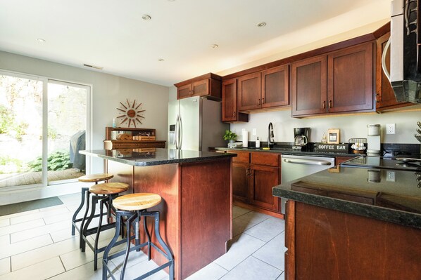 A modern kitchen with wooden cabinets, a large island with stools, and a coffee station.