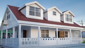 A two-story house with a red roof, white siding, and a covered porch with blue chairs.