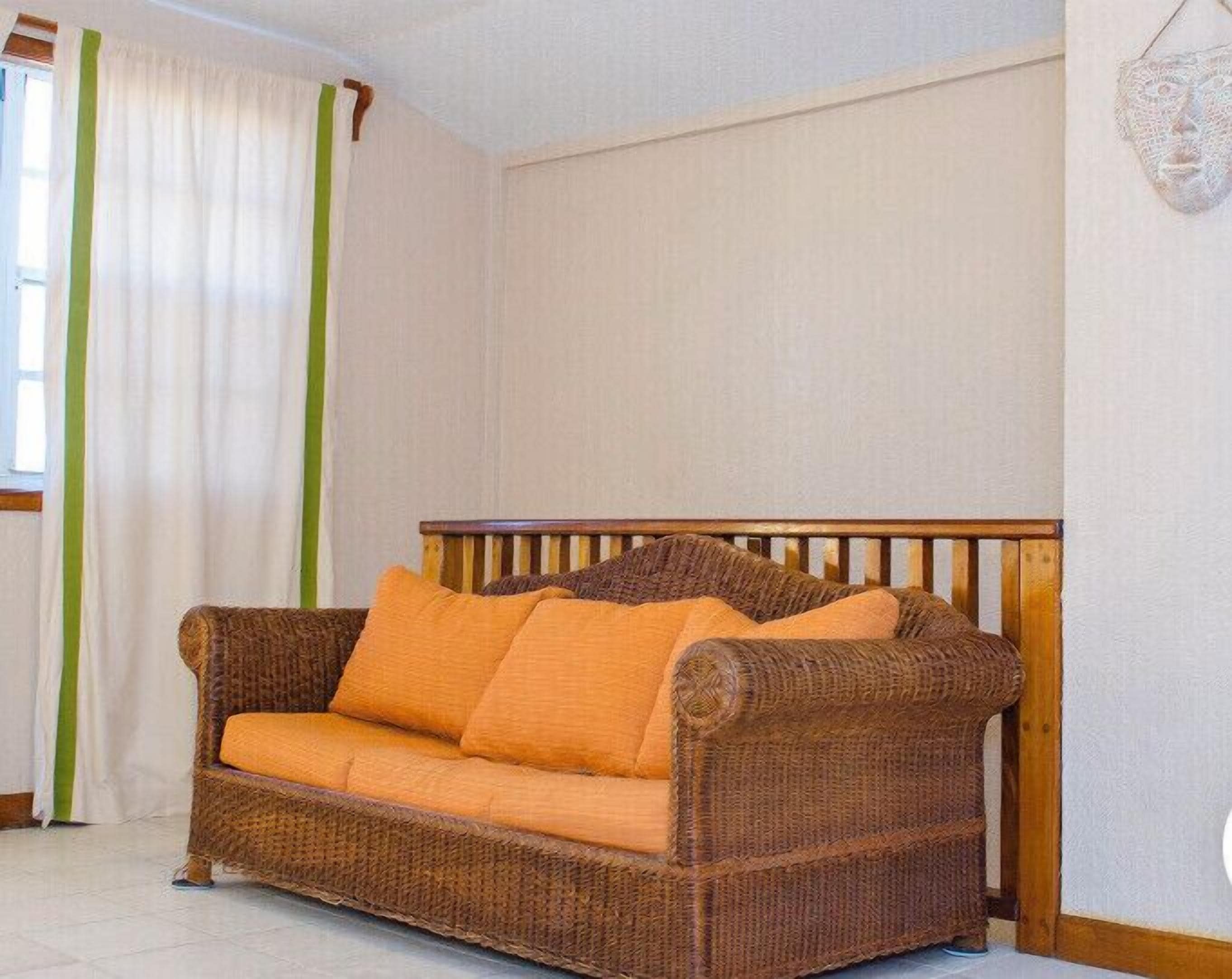 A wicker sofa with orange cushions in a room with white walls and a wooden headboard.