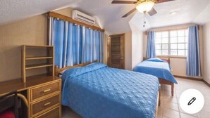 A bedroom with two beds, a ceiling fan, a window with curtains, and a wooden dresser.