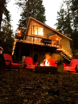 Uma cabana com varanda, lareira e cadeiras Adirondack vermelhas.