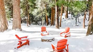 A snow-covered forest with four red Adirondack chairs arranged in a circle.