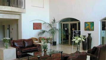 A spacious lobby with a leather sofa, a coffee table, and a red patterned rug. There are potted plants and a sign on the wall.