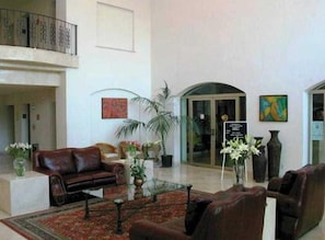A spacious lobby with a leather sofa, a coffee table, and a red patterned rug. There are potted plants and a sign on the wall. - Hg Hotel (Zapopan)