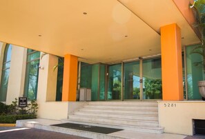 A building entrance with a glass facade, steps leading up to the entrance, and a sign indicating a lower level. - Hg Hotel (Zapopan)