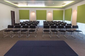 A conference room with rows of chairs, a stage with a green backdrop, and a carpeted floor. - Hg Hotel (Zapopan)