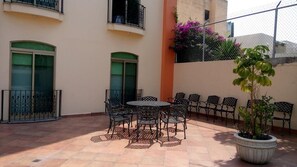 An outdoor patio with a round table and chairs, surrounded by a low fence and potted plants. - Hg Hotel (Zapopan)