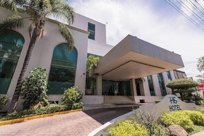 A modern hotel entrance with a covered walkway, palm trees, and a sign indicating the hotel name. - Hg Hotel (Zapopan)