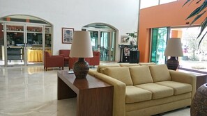A lobby with a sofa, two lamps, a table, and a glass door leading to a dining area.