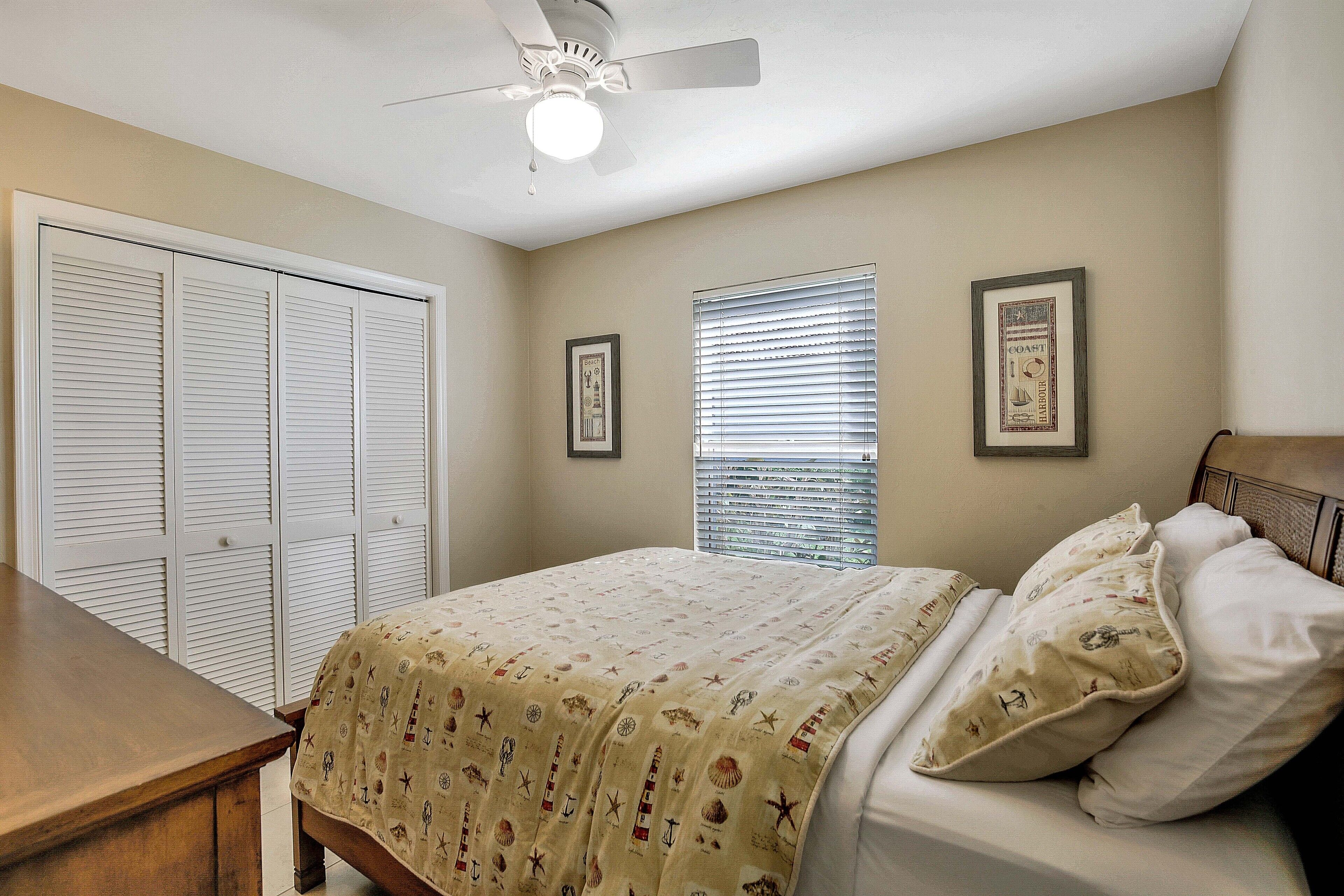 A bedroom with a bed, a wooden nightstand, a ceiling fan, and a window with blinds.