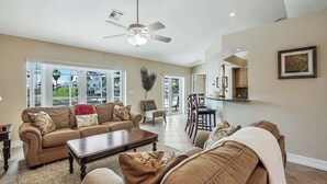 A spacious living room with a large sofa, a coffee table, and a ceiling fan. There is a dining area with a table and chairs visible in the background. - RARE Waterfront Western Exposure Vacation Home - Best Sunset Views & FREE WiFi (Marco Island)
