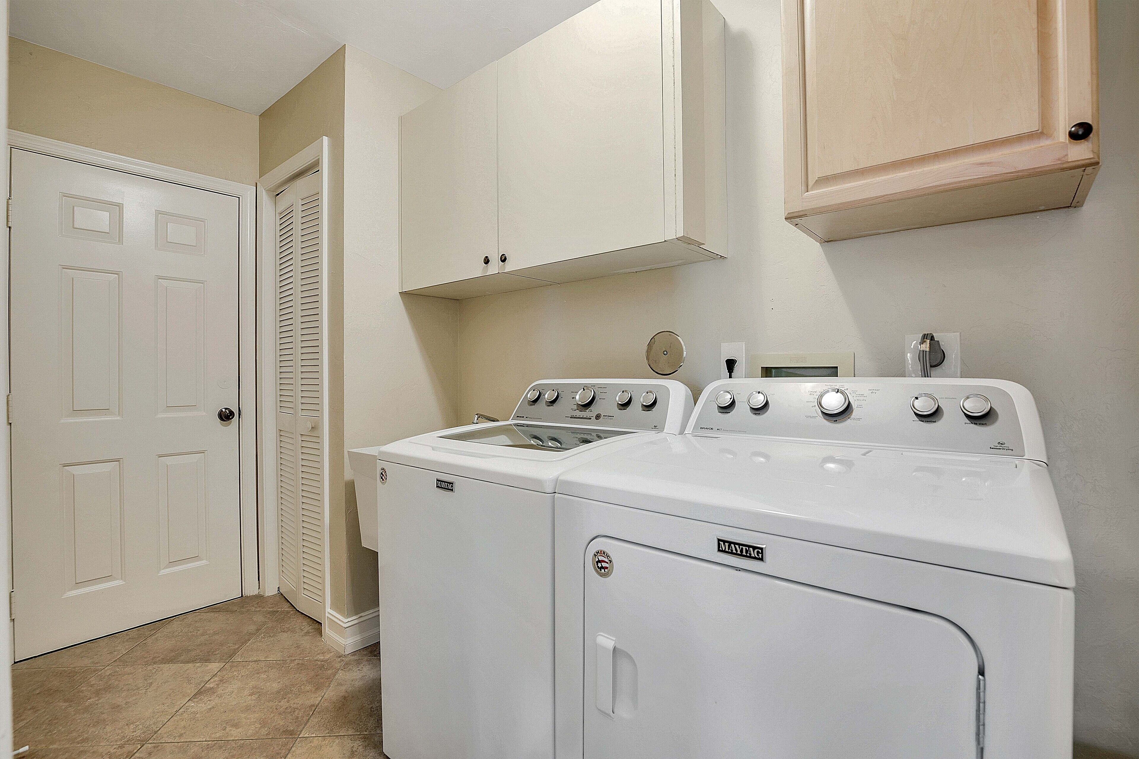 A laundry room with two stacked washers and dryers, a white door, and a wooden cabinet above.
