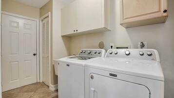 A laundry room with two stacked washers and dryers, a white door, and a wooden cabinet above.