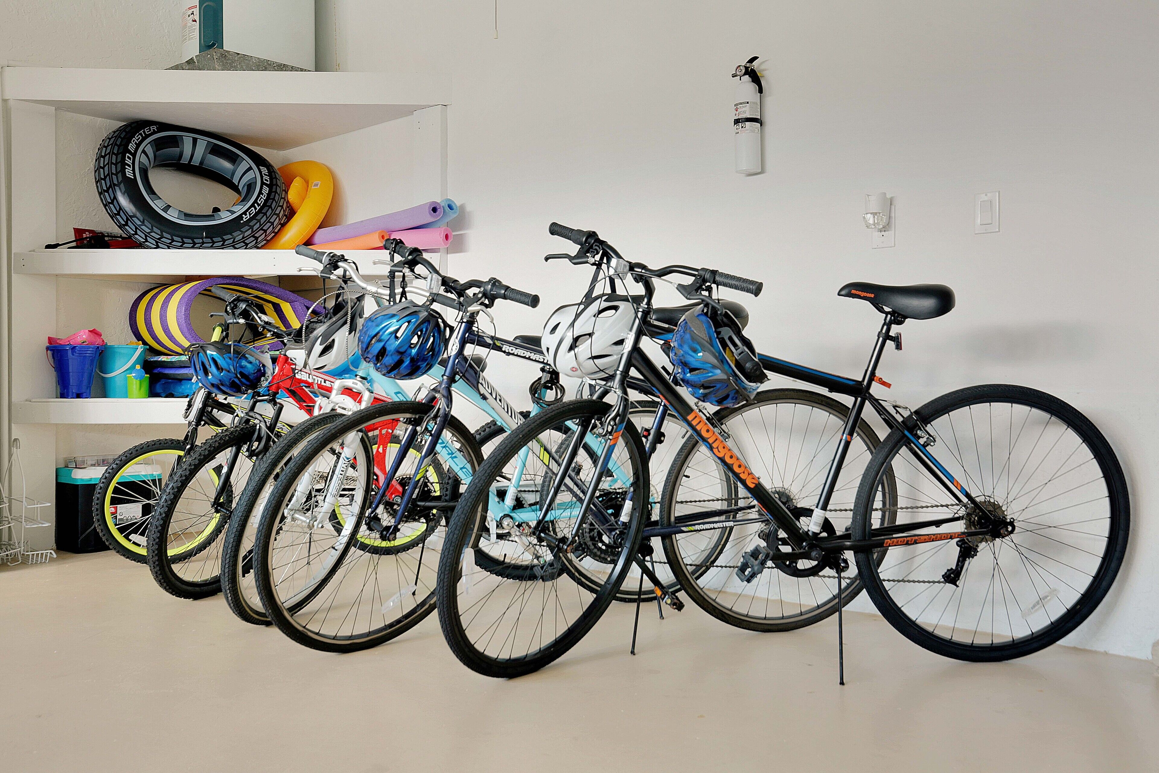 Bicycles parked in a room with a white wall, a shelf with tires and other items, and a fire extinguisher mounted on the wall.