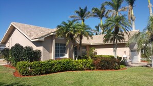 A two-story house with a tiled roof, surrounded by well-maintained hedges and palm trees. - RARE Waterfront Western Exposure Vacation Home - Best Sunset Views & FREE WiFi (Marco Island)