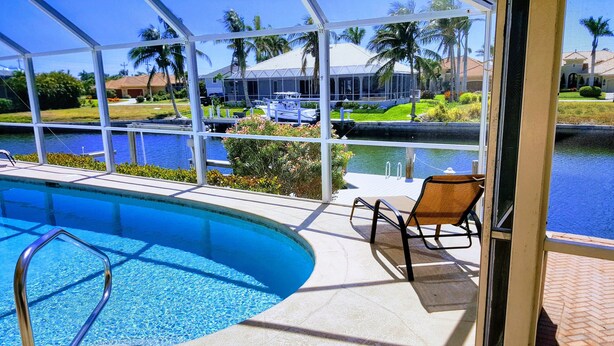 A swimming pool with a view of a house and palm trees. - RARE Waterfront Western Exposure Vacation Home - Best Sunset Views & FREE WiFi (Marco Island)