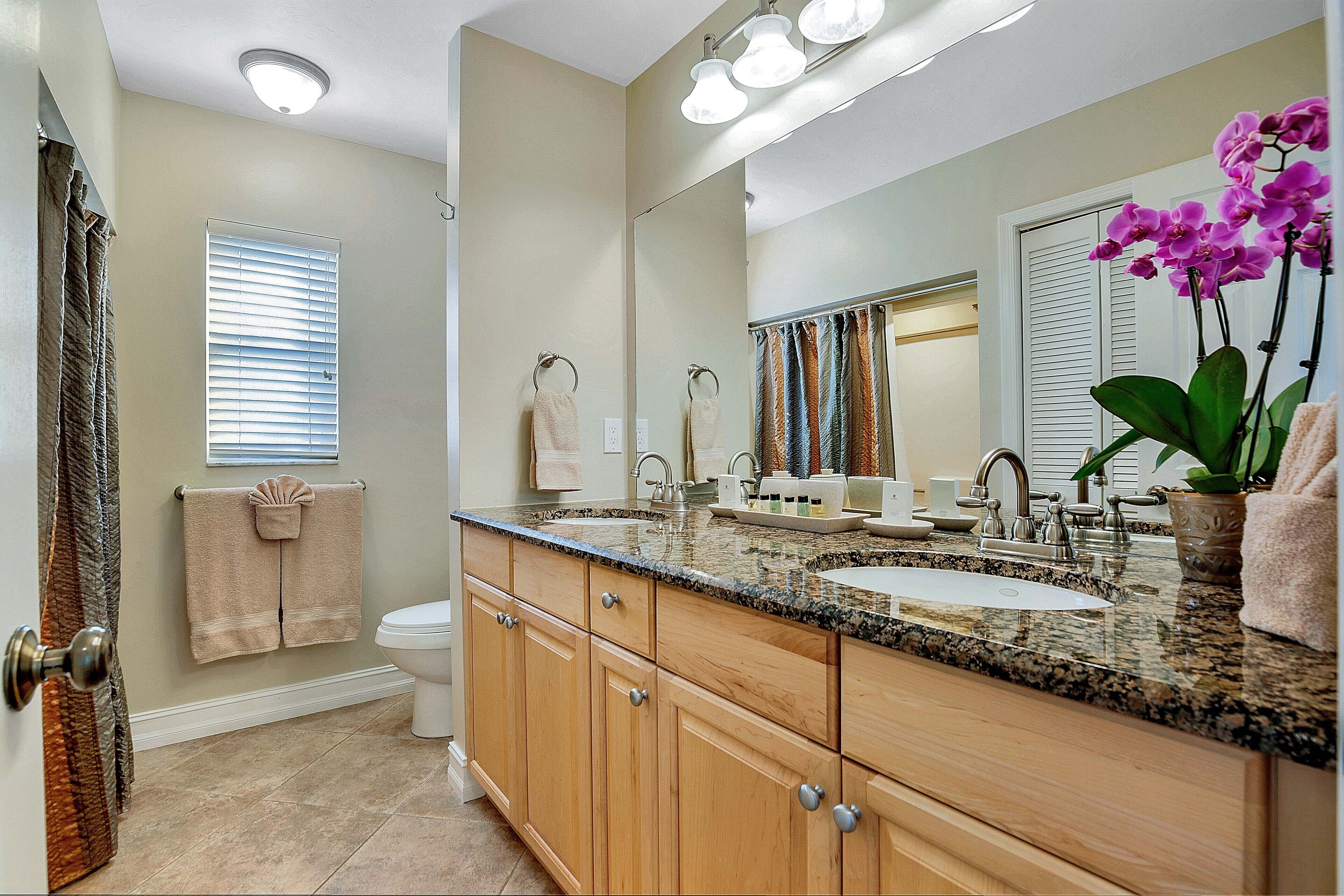 Une salle de bain avec un meuble-lavabo à deux vasques, un grand miroir et une orchidée en pot.