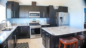 A modern kitchen with dark cabinetry, stainless steel appliances, a marble island, and a built-in oven. - 4X4 beach. Private Pool opens in May (Corolla)