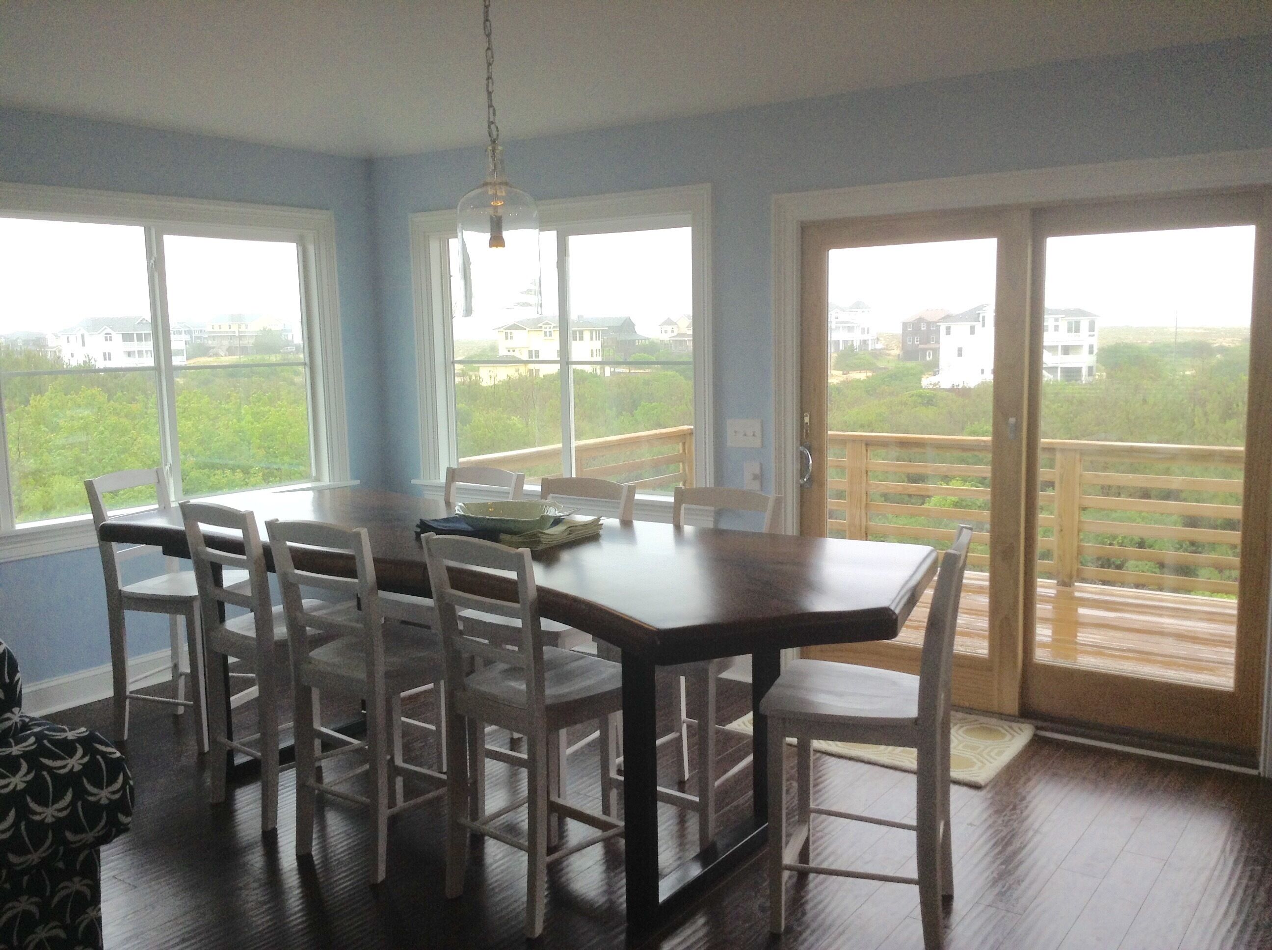 A dining area with a table and chairs, large windows, and a view of houses.